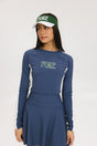 A female model wearing a long sleeve activewear top in blue and white with the text 'FORE' on the front, paired with a matching skirt and a visor with the text 'FORE'.