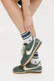 A person wearing green and blue striped retro ankle socks with a logo on the side, paired with white socks and green sneakers.