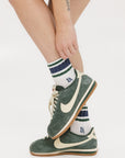 A person wearing green and blue striped retro ankle socks with a logo on the side, paired with white socks and green sneakers.