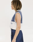 A model wearing an indigo and white intarsia mock neck, sleeveless Fore Sweater.