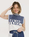A model wearing an indigo and white intarsia mock neck, sleeveless Fore Sweater.