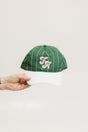 A green baseball cap with pinstripe detailing and an embroidered logo held in a hand against a white background.