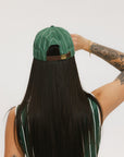 A person viewed from behind wearing a green striped hat with a brown band.