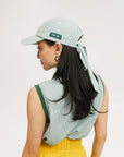 A woman wearing a green seersucker baseball cap with 'Chasing Balls' text embroidered on it and an oversized bow at the back.