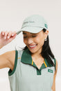 A woman wearing a green seersucker baseball cap with 'Chasing Balls' text embroidered on it and an oversized bow at the back.