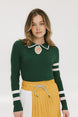 A woman wearing a green ribbed keyhole polo with white stripe accents on the sleeves and a gold smiley face button at the center front neck, paired with a yellow and white skirt.