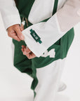 A woman wearing a long-sleeved green and pink warm-up jacket with a hood, zipper pockets, and colorblocking. She also sports a matching green cap and appears to be standing against a white background.