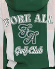 A woman wearing a long-sleeved green and pink warm-up jacket with a hood, zipper pockets, and colorblocking. She also sports a matching green cap and appears to be standing against a white background.