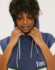 A person wearing a sleeveless hoodie with the hood up, featuring a mainly blue color with green and white accents, and the brand name 'Fore' visible.