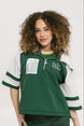 A woman wearing a green and white hoodie with a half-zip design, kangaroo pocket, and decorative woven ribbons.