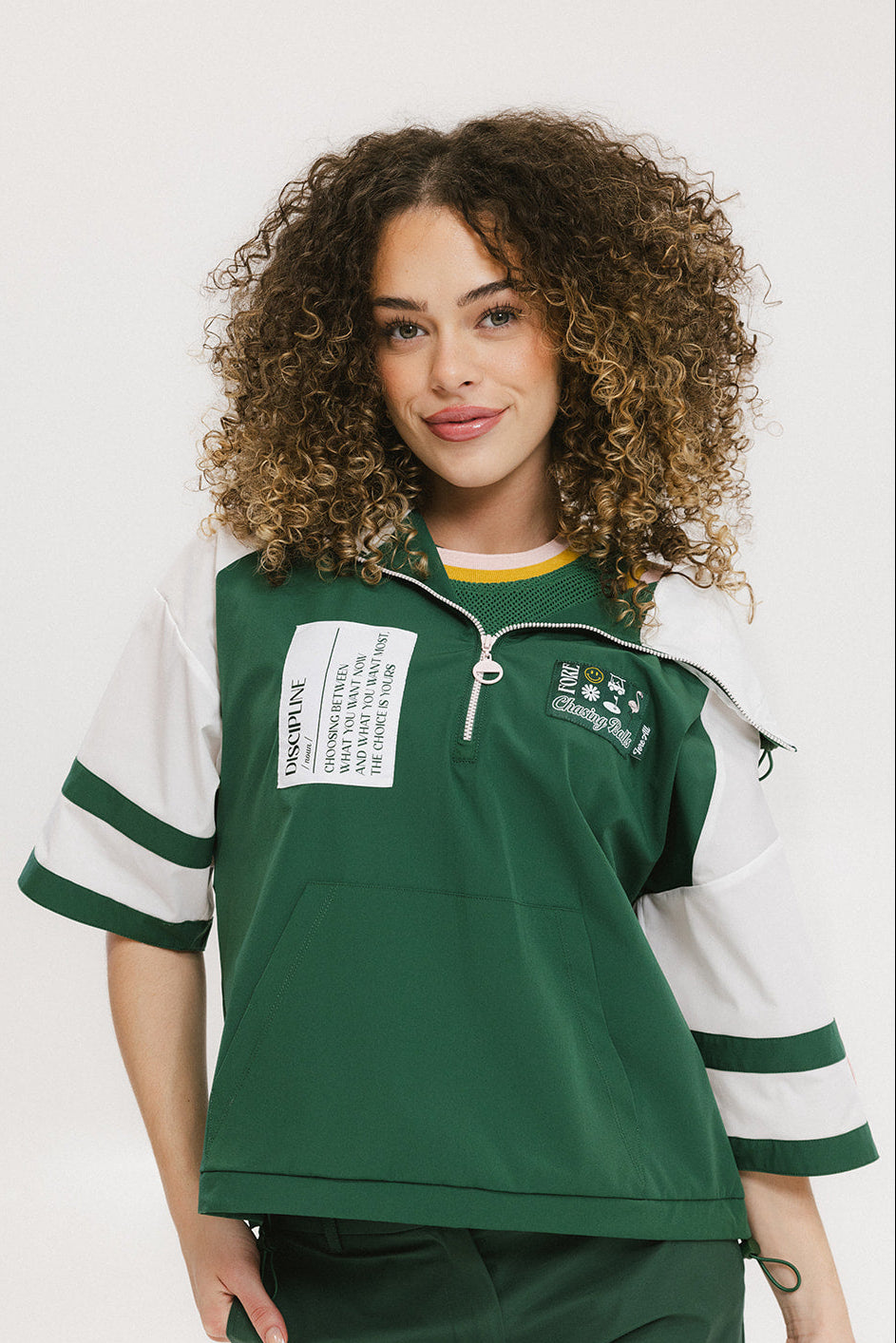 A woman wearing a green and white hoodie with a half-zip design, kangaroo pocket, and decorative woven ribbons.