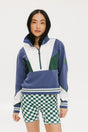 A woman wearing a half zip sports top with colorblocking in blue, white, and green, and ribbed detailing around the collar, cuffs, and hem.