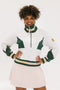 A woman wearing a white half zip sports top with green color blocking and ribbed detailing around the collar, cuffs, and hem. The top features half sleeve design with a signature logo on the chest.