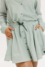 Model wearing the patty skirt in green seersucker. Featuring a green drawstring, buttons down the front, and a fore all logo on the bottom of the skirt.