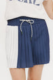 A pleated skirt with colorblocking in indigo and white, featuring a round drawstring cord at the waist and a 'Chasing Balls' icon patch on the back.