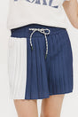 A pleated skirt with colorblocking in indigo and white, featuring a round drawstring cord at the waist and a 'Chasing Balls' icon patch on the back.