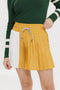 A person wearing a mustard pleated skirt with colorblocking, featuring a round drawstring cord and pockets.