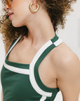 A woman wearing a green sleeveless dress with white accents and a round drawstring cord.