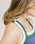 A woman is standing, wearing a sleeveless indigo dress with a round neckline, a drawstring at the waist, and white sneakers.