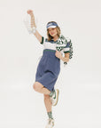 A woman wearing a polo dress with a color block design in white and indigo, featuring a ribbed collar, placket, and cuffs. She also wears a matching cap and sneakers.