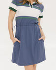 A woman wearing a polo dress with a color block design in white and indigo, featuring a ribbed collar, placket, and cuffs. She also wears a matching cap and sneakers.