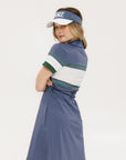A woman wearing a polo dress with a color block design in white and indigo, featuring a ribbed collar, placket, and cuffs. She also wears a matching cap and sneakers.