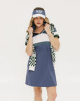A woman wearing a polo dress with a color block design in white and indigo, featuring a ribbed collar, placket, and cuffs. She also wears a matching cap and sneakers.
