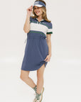 A woman wearing a polo dress with a color block design in white and indigo, featuring a ribbed collar, placket, and cuffs. She also wears a matching cap and sneakers.