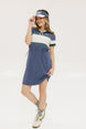 A woman wearing a polo dress with a color block design in white and indigo, featuring a ribbed collar, placket, and cuffs. She also wears a matching cap and sneakers.