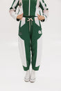 A pair of color-blocked green and white warm-up pants with a pink stripe, featuring a flat drawstring waistband and deep front pockets, branded with the 'Fore All' detail on the back and an FA icon on the inner calf.