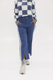 A person wearing the Simone Pant in blue with white stripes on the side, featuring princess seams down the leg and a slit at the hem. The person is also wearing a checkered blue and white top and white sneakers.
