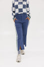 A person wearing the Simone Pant in blue with white stripes on the side, featuring princess seams down the leg and a slit at the hem. The person is also wearing a checkered blue and white top and white sneakers.