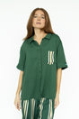 A woman wearing a green button-up shirt with a collar and front pocket, paired with striped pants.