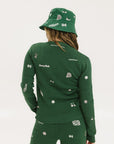 A woman wearing a green knit sweater with embroidered icons, matching green bucket hat, and green pants.