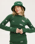 A woman wearing a green knit sweater with embroidered icons, matching green bucket hat, and green pants.
