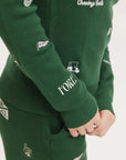 A woman wearing a green knit sweater with embroidered icons, matching green bucket hat, and green pants.