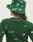 A woman wearing a green knit sweater with embroidered icons, matching green bucket hat, and green pants.