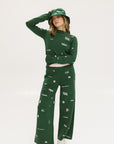 A woman wearing a green knit sweater with embroidered icons, matching green bucket hat, and green pants.