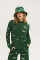 A woman wearing a green knit sweater with embroidered icons, matching green bucket hat, and green pants.