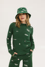 A woman wearing a green knit sweater with embroidered icons, matching green bucket hat, and green pants.