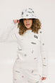 A woman wearing a white crew neck sweater with embroidered icons, matching white shorts, and a white bucket hat with a logo.