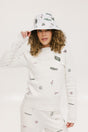 A woman wearing a white crew neck sweater with embroidered icons, matching white shorts, and a white bucket hat with a logo.