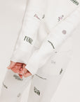 A woman wearing a white crew neck sweater with embroidered icons, matching white shorts, and a white bucket hat with a logo.