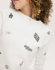 A woman wearing a white crew neck sweater with embroidered icons, matching white shorts, and a white bucket hat with a logo.