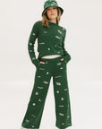 A woman wearing a green bucket hat with embroidered icons, matching green pants, and white shoes.