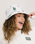 A person wearing a white bucket hat with green embroidered icons.