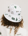 A person wearing a white bucket hat with green embroidered icons.