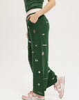A pair of green Kennedy pants with embroidered icons, paired with a green top and pink shoes.