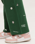 A pair of green Kennedy pants with embroidered icons, paired with a green top and pink shoes.