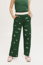 A pair of green Kennedy pants with embroidered icons, paired with a green top and pink shoes.